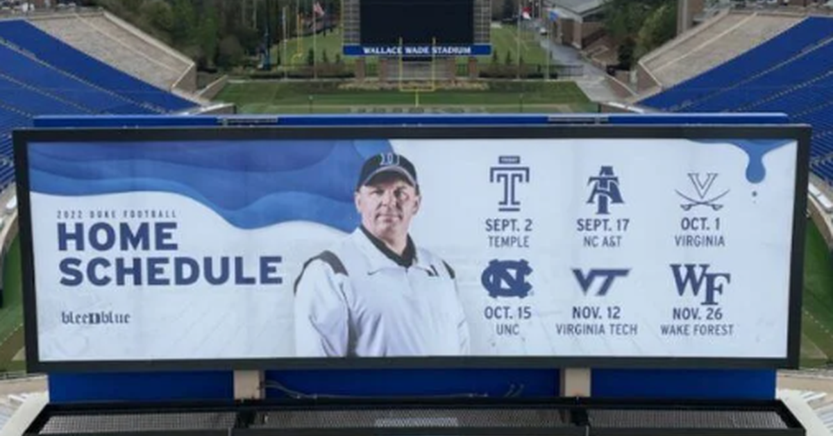 An aerial view of a billboard installed at the end of the field of a large stadium while dark clouds roll overhead.