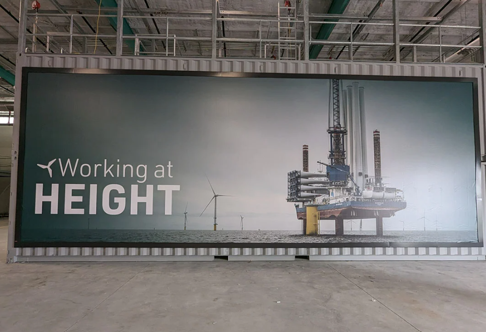A large indoor wall graphic shows offshore wind turbines and a platform with the words "Working at Height."