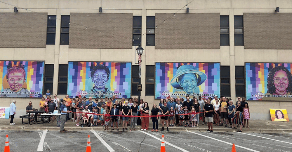 A colorful outdoor art display mounted on a building wall, featuring a large framed mural with abstract shapes and vivid patterns.