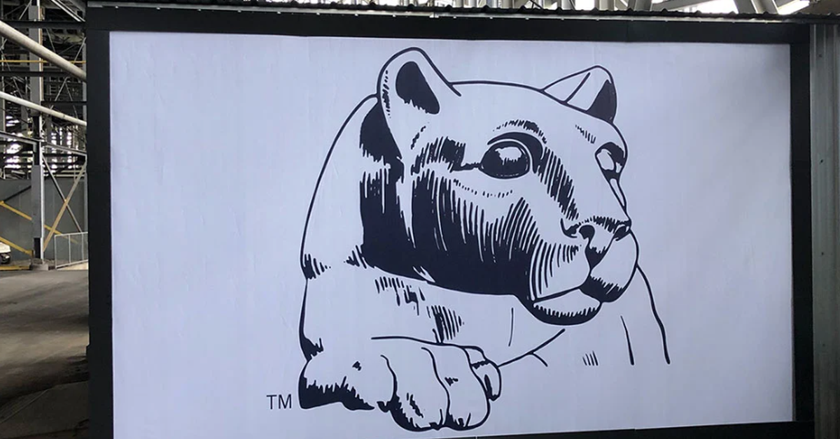 A large black-and-white wildcat illustration is displayed on a wall inside a stadium area during the daytime.