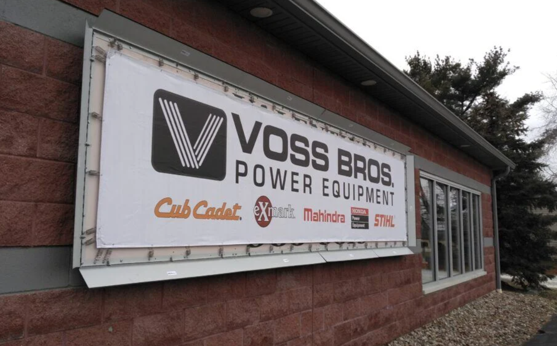 A large Voss Bros. Power Equipment sign is mounted on a brick building beside windows and landscaping stones.