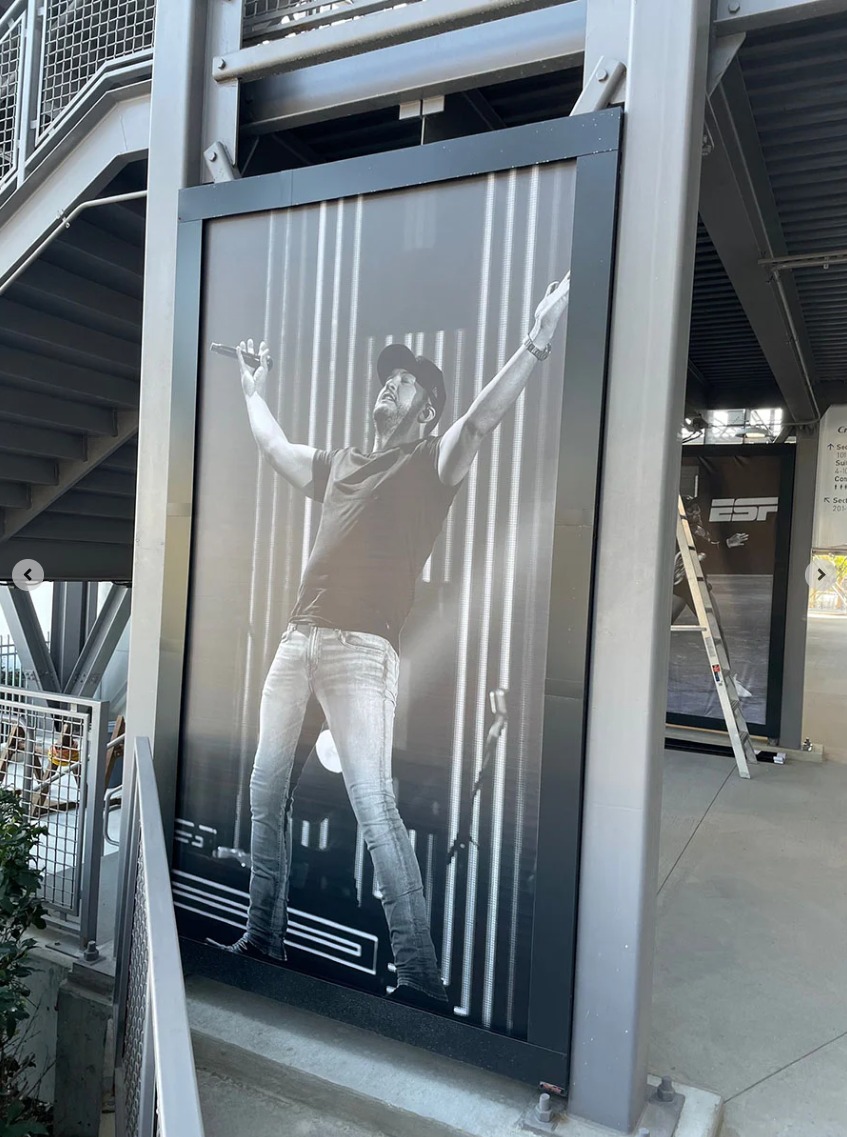 A large black-and-white wall display showing a singer holding a microphone under metal stairs and beams.