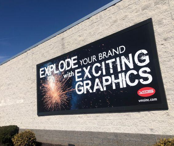 A black outdoor wall sign that says, "Elevate your brand with captivating graphics," is mounted on a brick building.