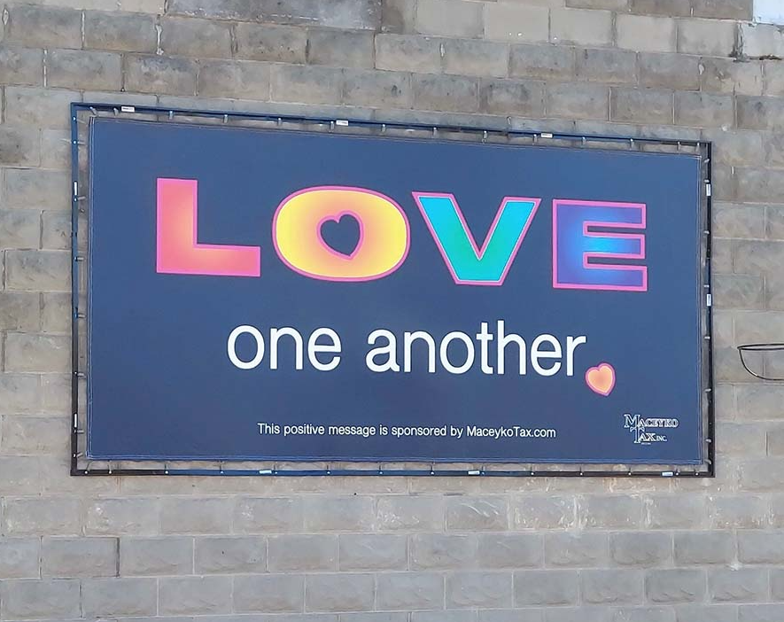 A dark banner on a block wall reads "Love one another," with colorful letters and small heart graphics.