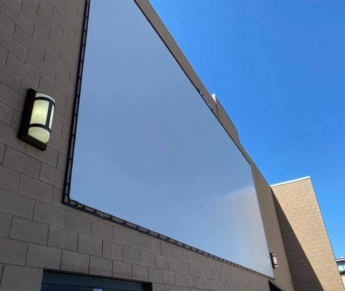 A large blank rectangular sign mounted on a block wall beneath a blue sky, with a light fixture nearby.