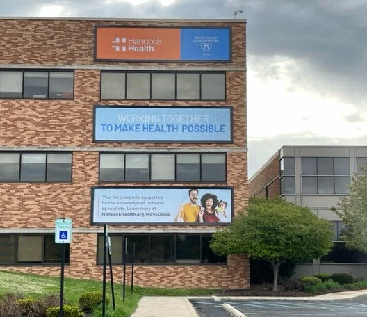 A brick medical office building with three large exterior signs above windows, landscaping, and a parking area.  Image B