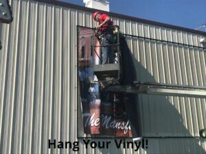vinyl-banner-being-hung-between-the-frames-on-the-siding-300x225 Lind SignSpring: Custom Banner Signs for Your Business