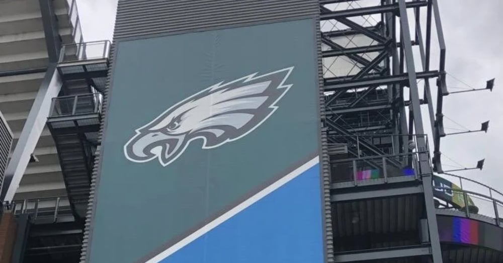 A large stadium sign displaying a white eagle logo on teal and blue panels beside metal seating supports.