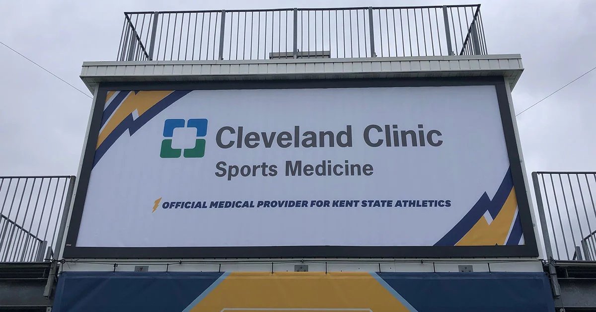 A stadium sign displaying Cleveland Clinic Sports Medicine branding above seats and railings under a gray sky.
