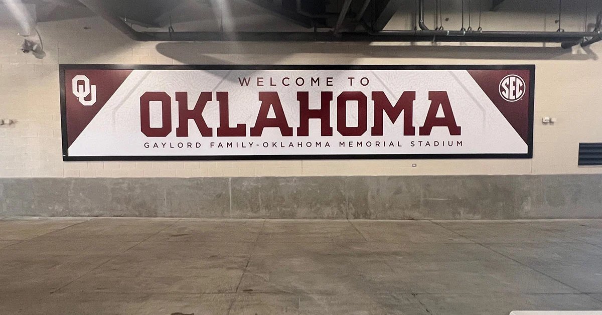 A wall sign reading Welcome to Oklahoma mounted above a concrete corridor with dark ceiling fixtures.