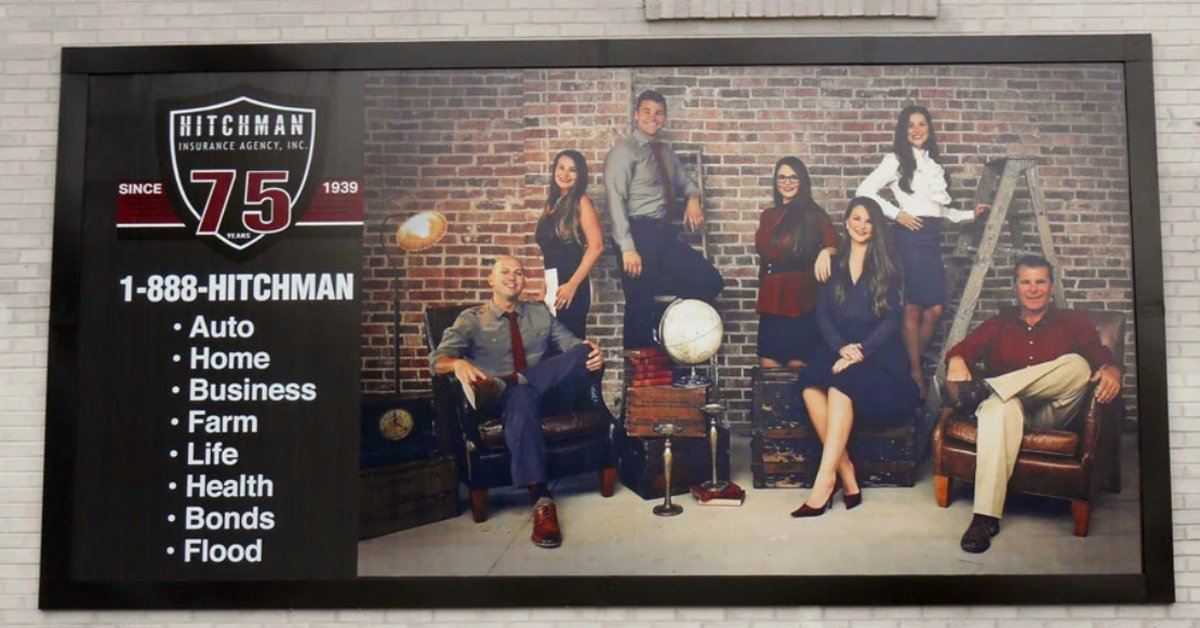 Large exterior business sign for an insurance agency displaying staff portraits, company branding, and a list of insurance services.