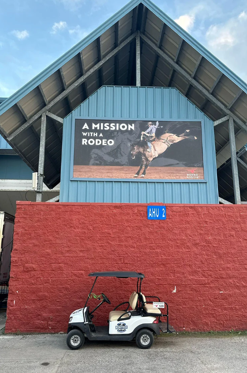 A low-angle view of a building with a rodeo sign above a brick wall and a small golf cart parked in front.