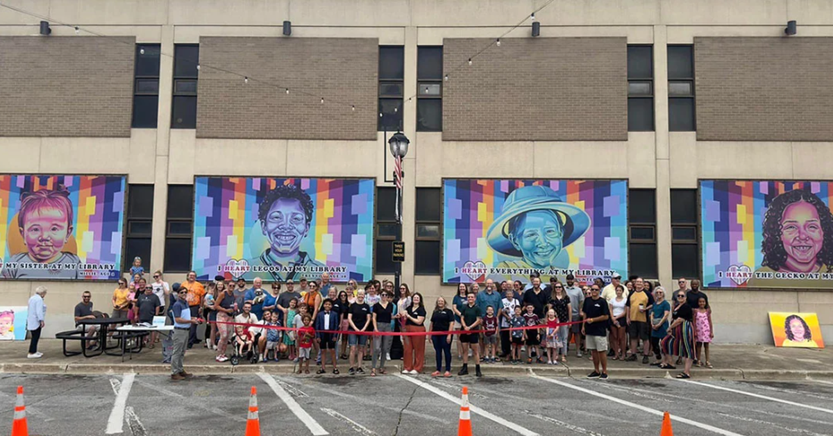 A colorful outdoor art display mounted on a building wall, featuring a large framed mural with abstract shapes and vivid patterns.