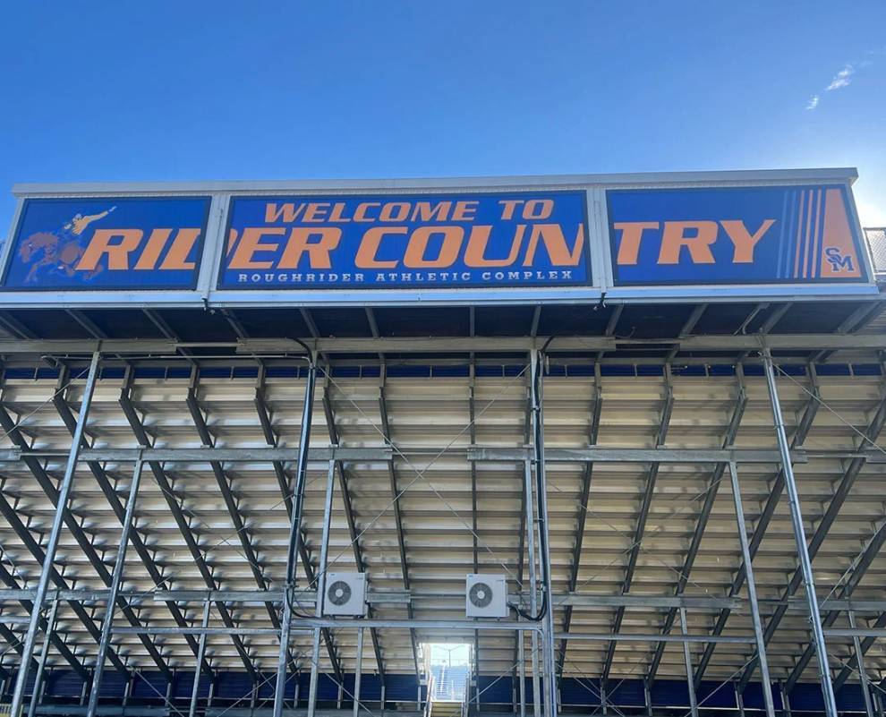 A large blue-and-orange stadium sign reading "Welcome to Rider Country" above metal bleachers and beams.