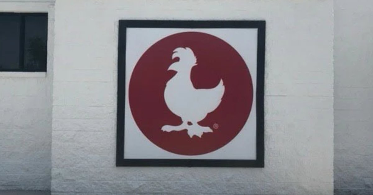 A framed sign featuring a white chicken silhouette inside a red circle mounted on a white brick exterior wall.