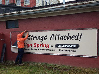 Lind worker hanging a Lind billboard that says "No Strings Attached!" on the side of the Lind main office building