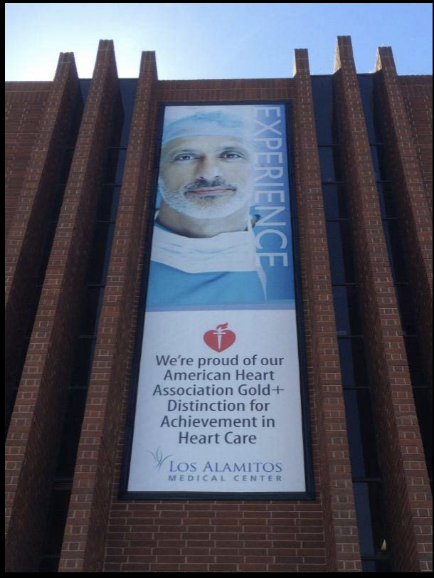 A Lind SignSpring Product – BannerFrameCLASSIC With Covers for Los Alamitos Medical Center on the exterior brick wall-Vertical Banner- “Experience” Design