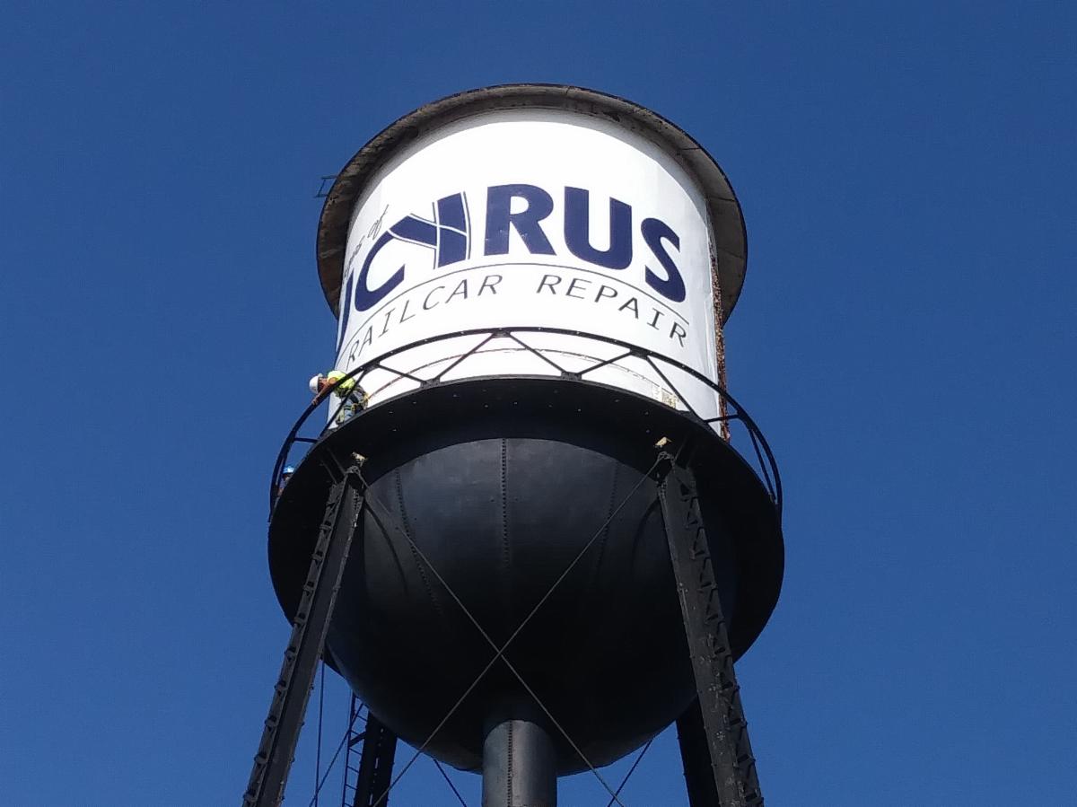 A Lind SignSpring Product – BannerFrameFLEX for Bucyrus Rail Car Repair On a Water Tower – Banner attached to the Rusty metal curved surface-After Photo