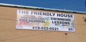 A Lind SignSpring Product – BannerFrameCLASSIC without Covers for Friendly House Swimming Lessons– A banner attached Exterior Brick School wall